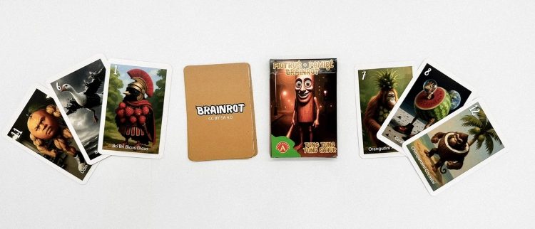 Pudełko gry Piotruś Brainrot Tung Sahur w centrum, otoczone rozłożonymi kartami z surrealistycznymi grafikami takimi jak Bombombini Gusini i Bri Bri Biccus Dicuus.