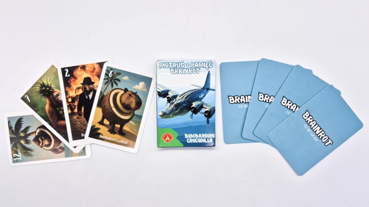 Pudełko gry Piotruś Brainrot Bombardiro Crocodillo otoczone stosem zakrytych kart i kilkoma odkrytymi kartami z surrealistycznymi grafikami.