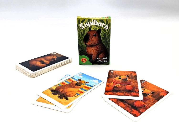 Pudełko gry "Piotruś Pamięć Kapibara" obok stosu kart i kilku rozłożonych kart z kapibarami.