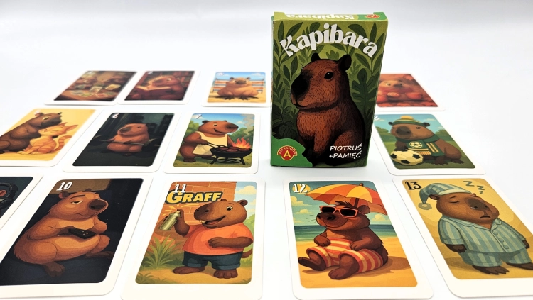 Pudełko gry "Piotruś Pamięć Kapibara" na białym tle, otoczone rozłożonymi kartami z ilustracjami kapibar.