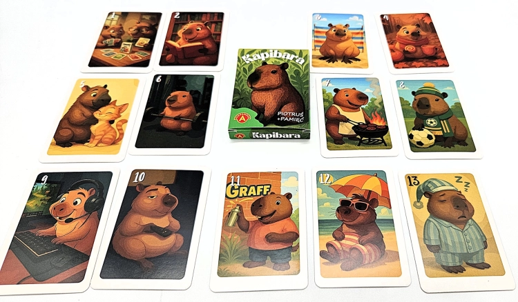 Pudełko gry "Piotruś Pamięć Kapibara" w centrum, otoczone rozłożonymi kartami z ilustracjami kapibar.