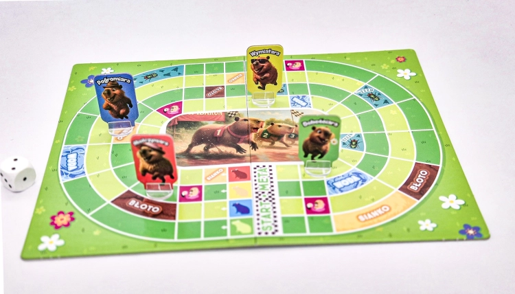 Plansza do gry "Kapibary na Start" z rozstawionymi pionkami kapibar i kostką do gry.