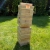 Wysoka, chwiejna wieża Jenga zbudowana z naturalnych drewnianych klocków z logo BeGame.pl, stojąca na trawie.
