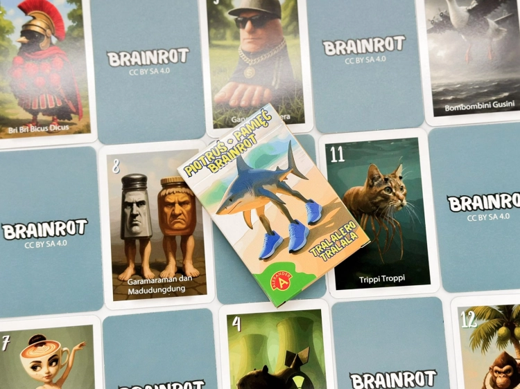 Opakowanie gry karcianej Piotruś Brainrot, otoczone rozłożonymi kartami na stole.