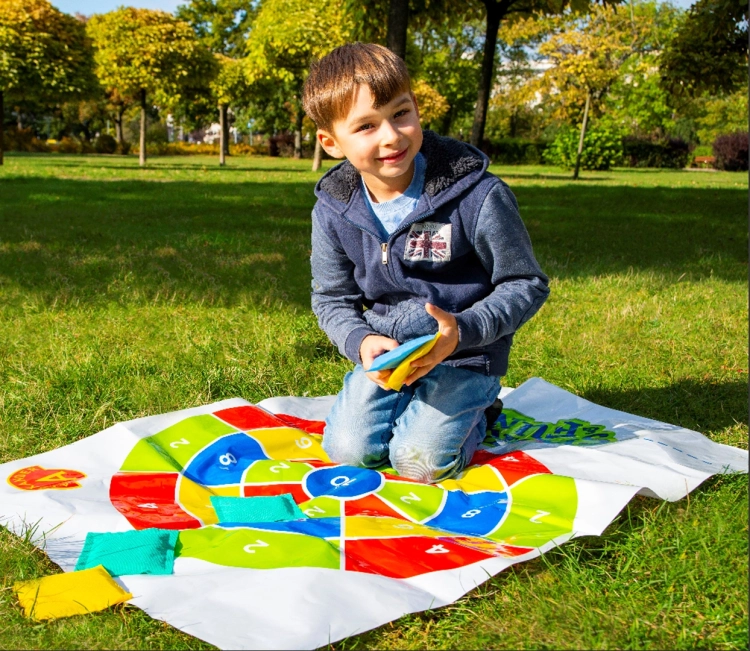 Chłopiec klęczy na trawie i przygotowuje się do rzutu woreczkami w grze "Strzał w 10".