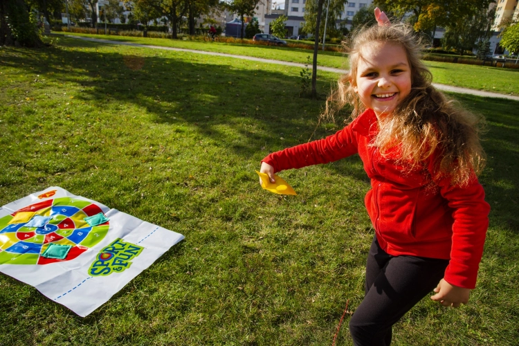 Uśmiechnięta dziewczynka rzuca woreczkiem w kolorową matę do gry "Strzał w 10".