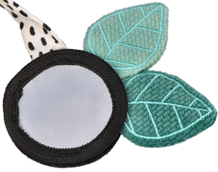 Zbiliżenie na element spirali edukacyjnej: lusterko dla niemowląt w czarnej ramce z miękkimi, teksturowanymi, miętowo-niebieskimi listkami.