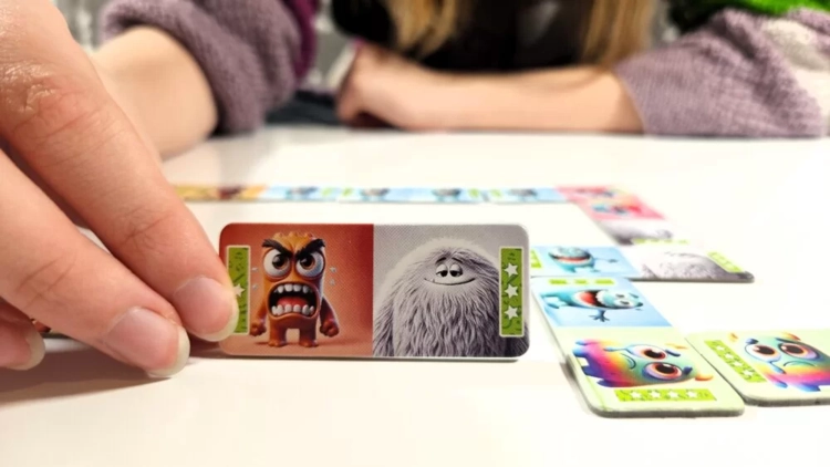 Dłoń dokłada element do ułożonego ciągu klocków, widoczny potwór zły i włochaty potwór z gry Domino Emocje.