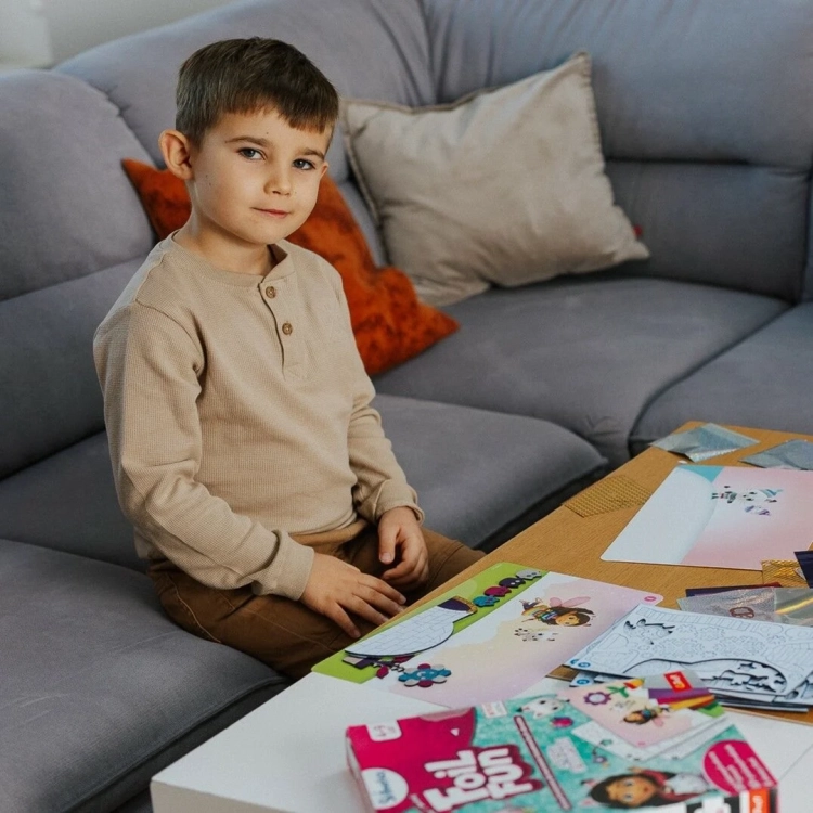 Chłopiec siedzi na sofie obok rozłożonego zestawu Foil Fun Gabby's Dollhouse.