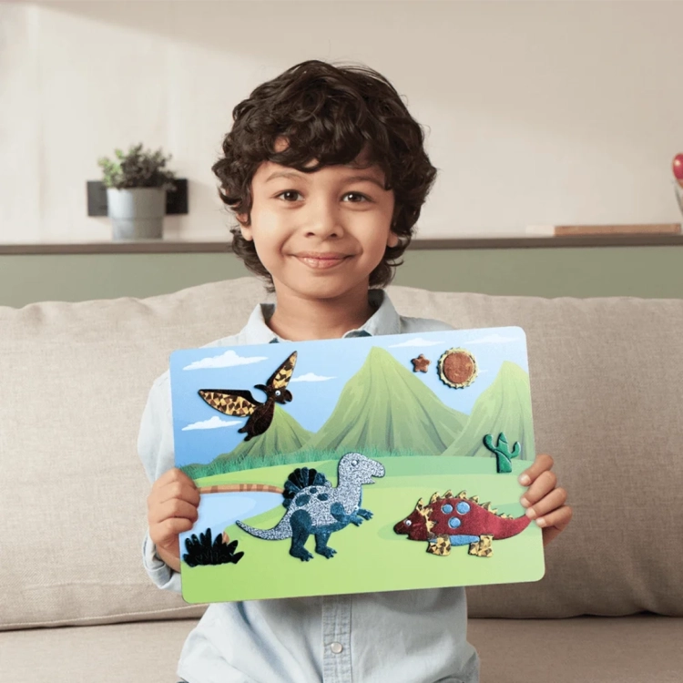 Zadowolony chłopiec trzyma ozdobiony folią obrazek z dinozaurami Skillmatics Foil Fun.