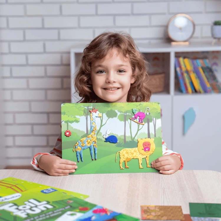 Uśmiechnięta dziewczynka trzyma gotowy obrazek z folii z żyrafą i lwem, z zestawu Foil Fun.