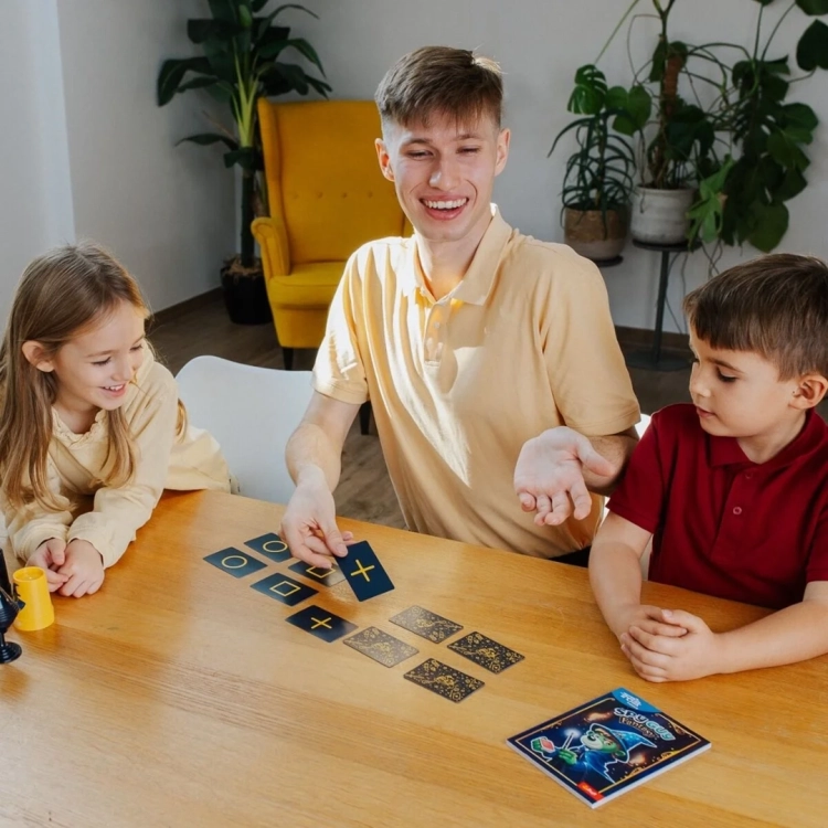 Dzieci uczą się magicznych sztuczek Spy Guy Fantasy, grając kartami na drewnianym stole.