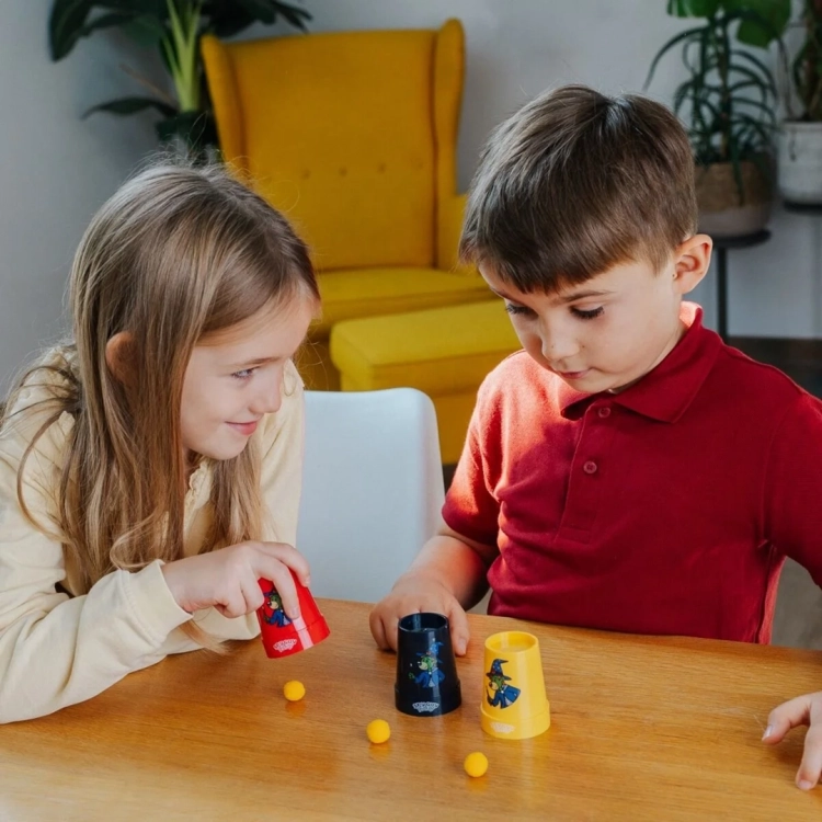 Dziewczynka i chłopiec grają w sztuczkę magiczną z kubeczkami i kulkami.