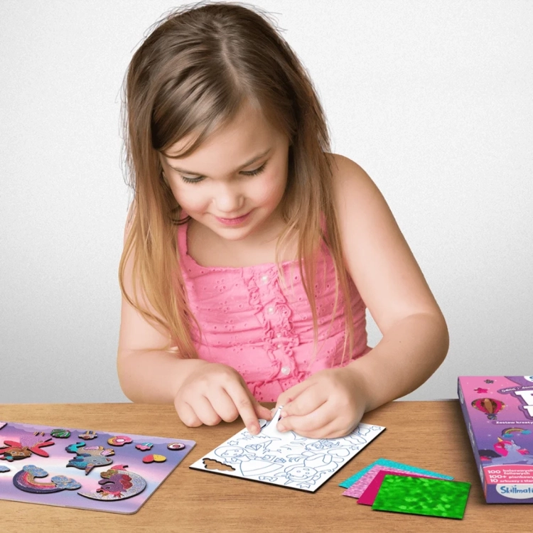 Dziewczynka odkleja warstwę ochronną z obrazka do foliowania Skillmatics Foil Fun Jednorożce i Księżniczki.