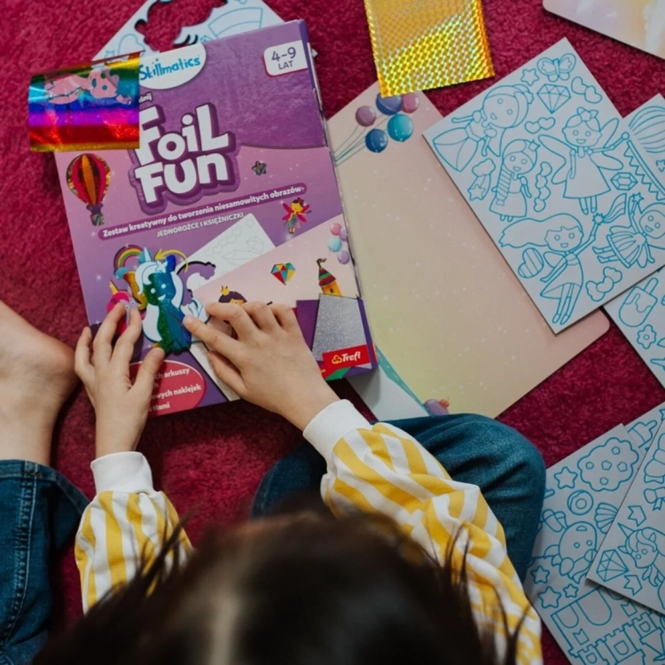 Dziecko bawi się zestawem Skillmatics Foil Fun na dywanie, korzystając z kolorowej folii i szablonów.