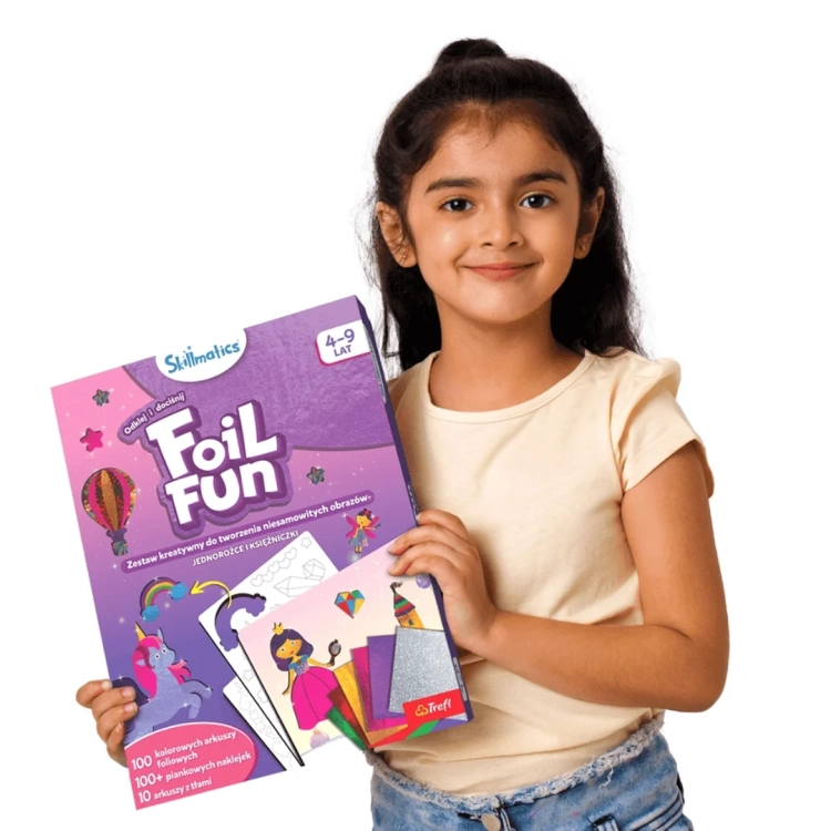 Uśmiechnięta dziewczynka trzyma w rękach pudełko Skillmatics Foil Fun Jednorożce i Księżniczki Trefl 4-9 lat.