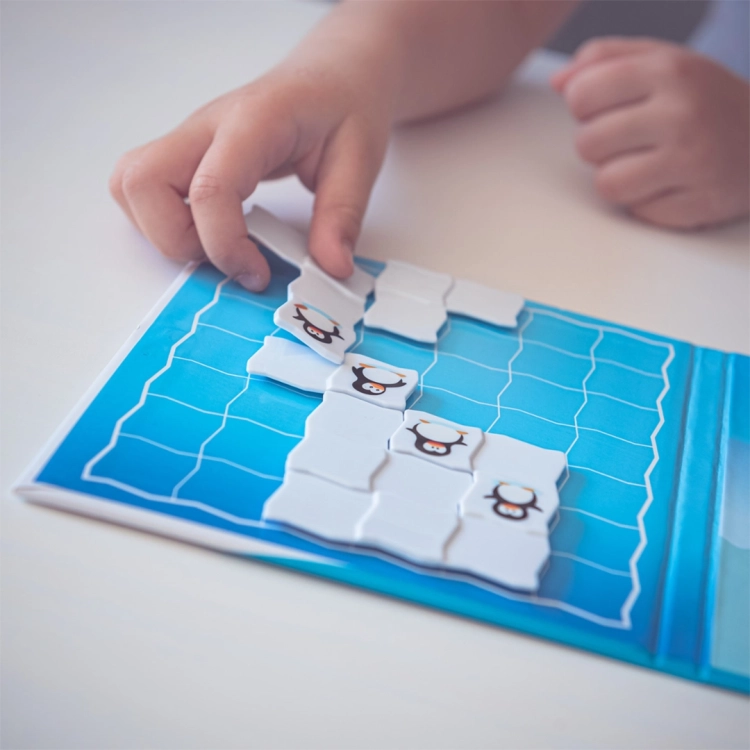 Dziecięce dłonie układają ostatni element lodu z pingwinem w grze Parada Pingwinów na planszy magnetycznej