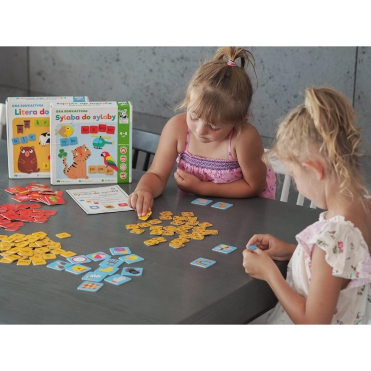 Dwie dziewczynki grają w grę edukacyjną Sylaba do sylaby Kapitan Nauka przy stole.