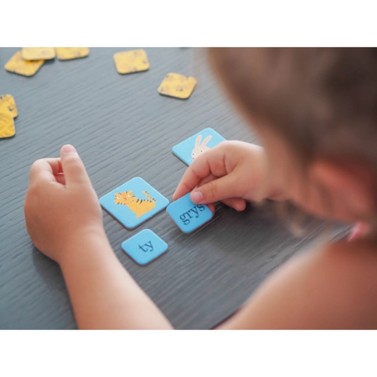 Zbliżenie na dłonie dziecka układającego słowo tygrys z sylab w grze edukacyjnej.