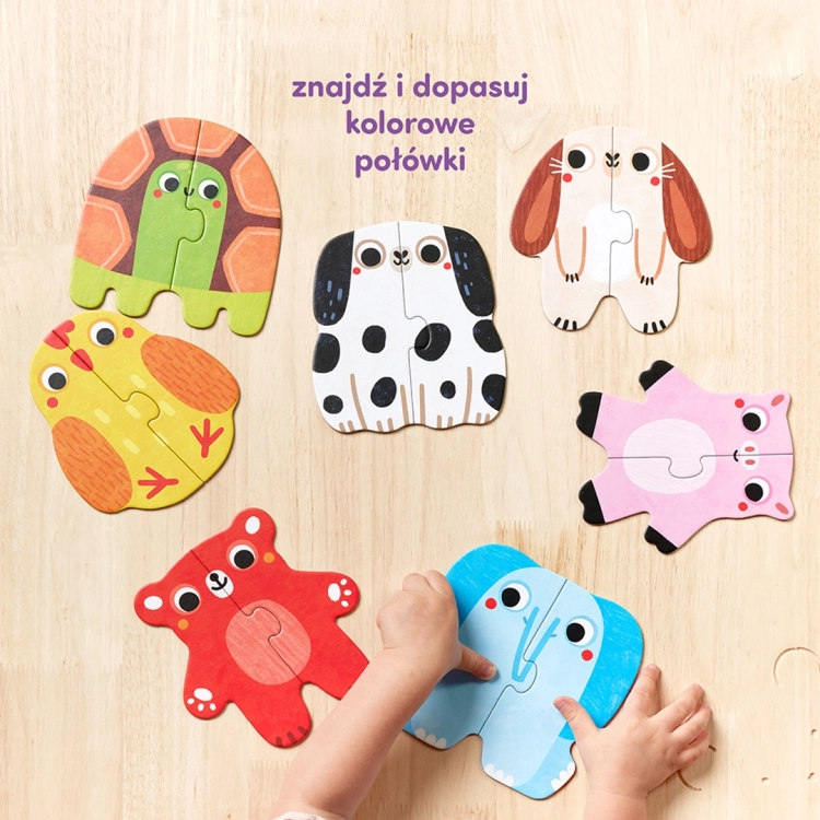 Dziecięce dłonie dopasowują dwie połówki niebieskiego słonia na drewnianym stole obok ułożonych puzzli z innymi zwierzętami.