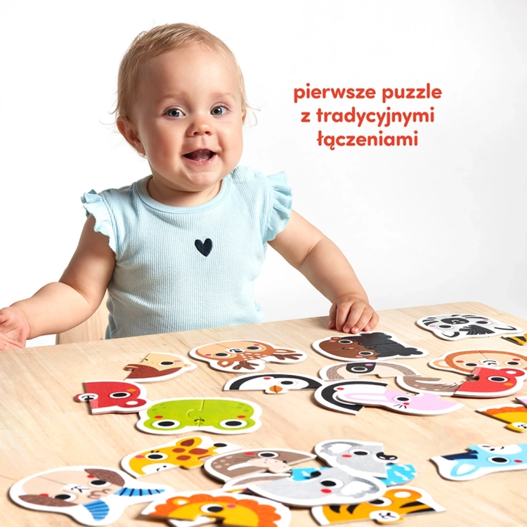 Małe dziecko siedzi przy drewnianym stole, na którym rozłożone są kolorowe, dwuelementowe puzzle przedstawiające buzie zwierząt i ludzi.