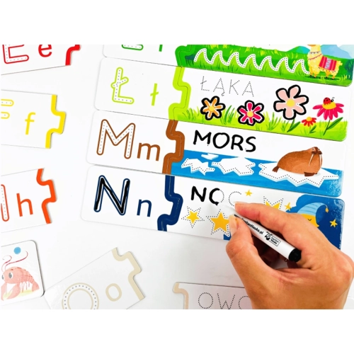 Zbliżenie na dłoń piszącą mazakiem po puzzlach z literą N i słowem "noc" na tle gwieździstego nieba.