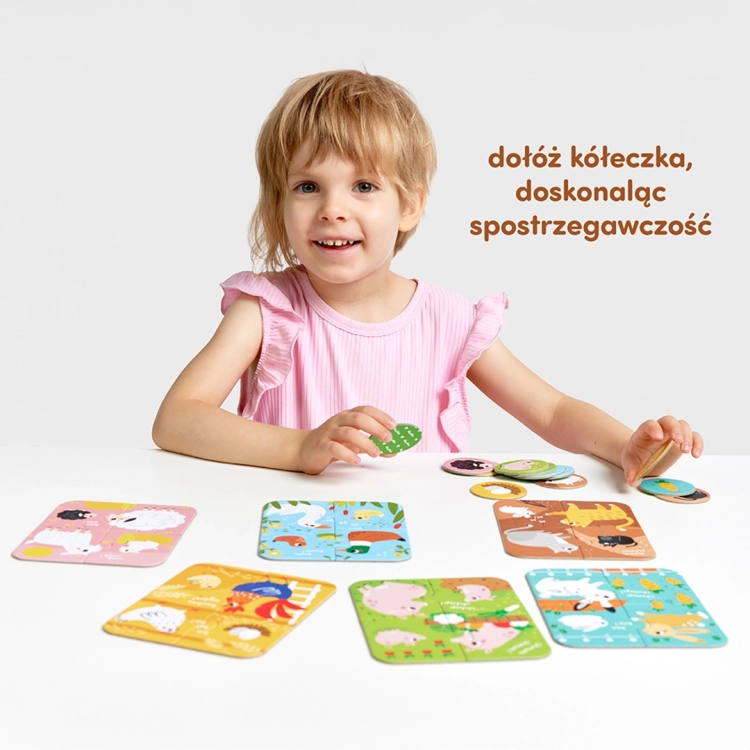 Uśmiechnięte dziecko siedzi przy białym stole, na którym rozłożone są kolorowe układanki z wiejskimi zwierzętami oraz pasujące do nich żetony.