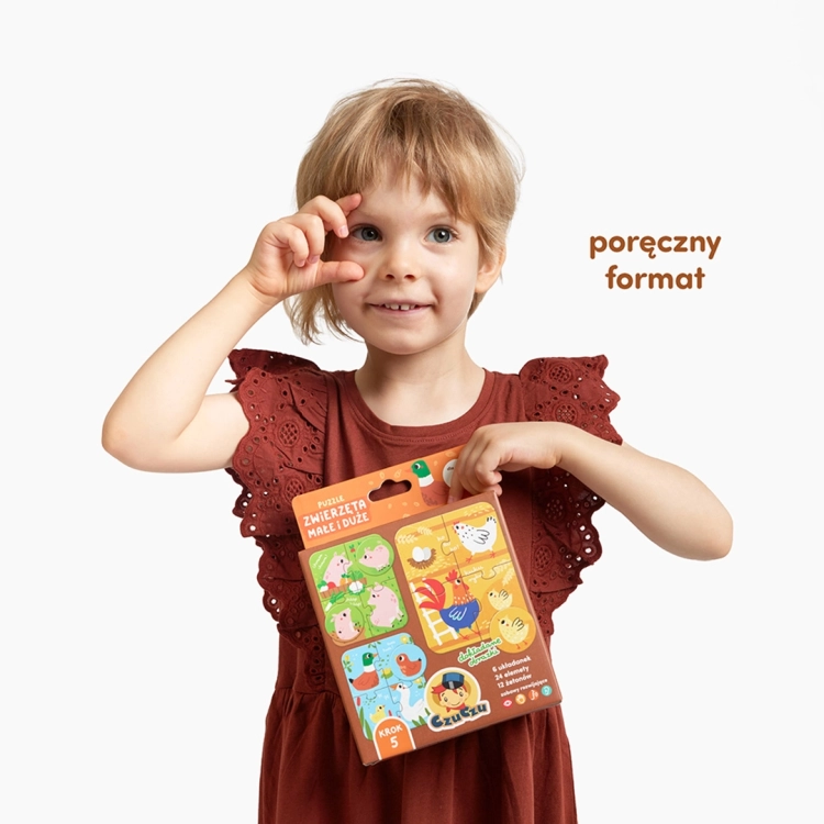 Małe dziecko w bordowej sukience trzyma w rękach brązowe opakowanie puzzli CzuCzu „Zwierzęta małe i duże”.