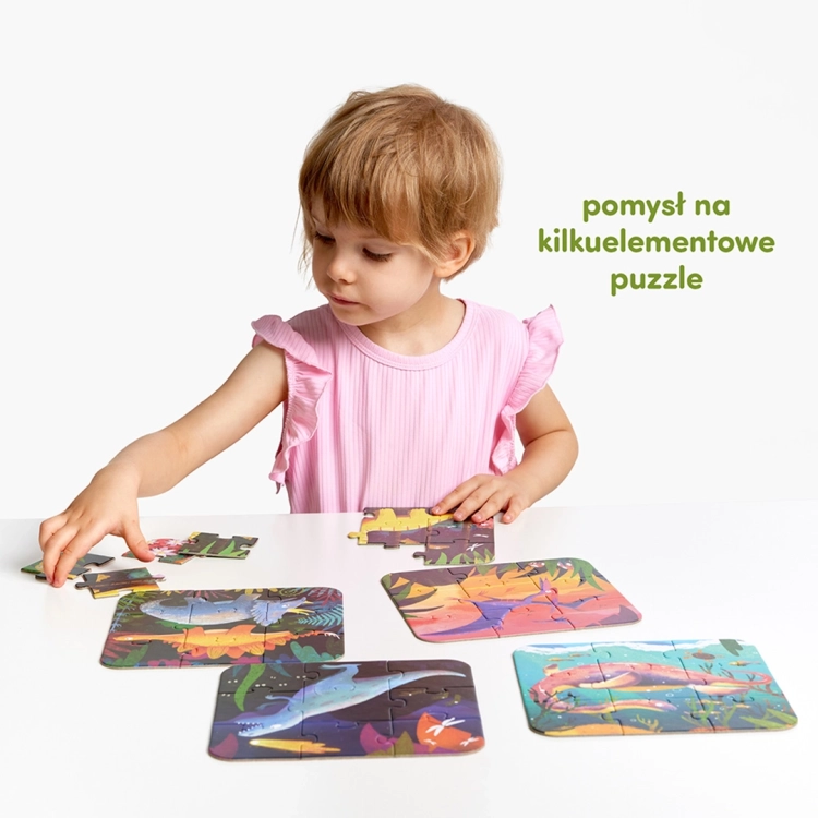 Mała dziewczynka w różowej bluzce siedzi przy białym stole, na którym układa kolorowe puzzle z dinozaurami.