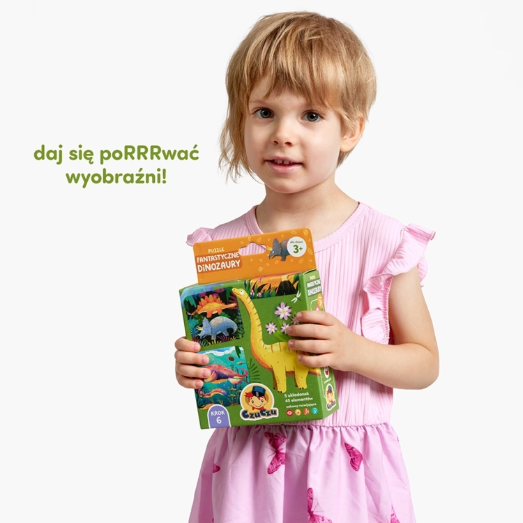Dziewczynka uśmiecha się, trzymając w rękach zielone pudełko puzzli edukacyjnych CzuCzu „Fantastyczne dinozaury”.