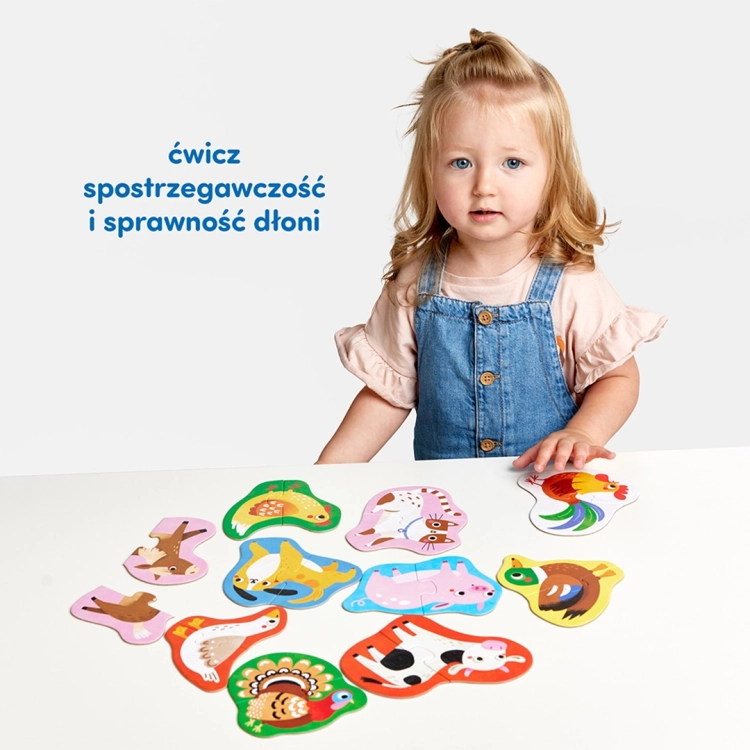 Dziewczynka w dżinsowych ogrodniczkach prezentuje na białym stole zestaw dziesięciu ułożonych układanek ze zwierzętami.