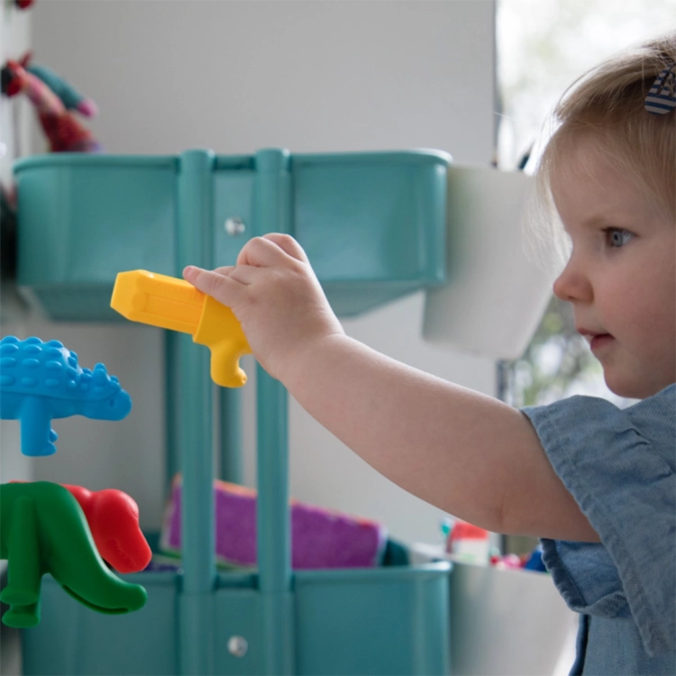 Dziewczynka bawi się magnetycznymi figurkami dinozaurów, przyczepiając żółty element do metalowego regału.