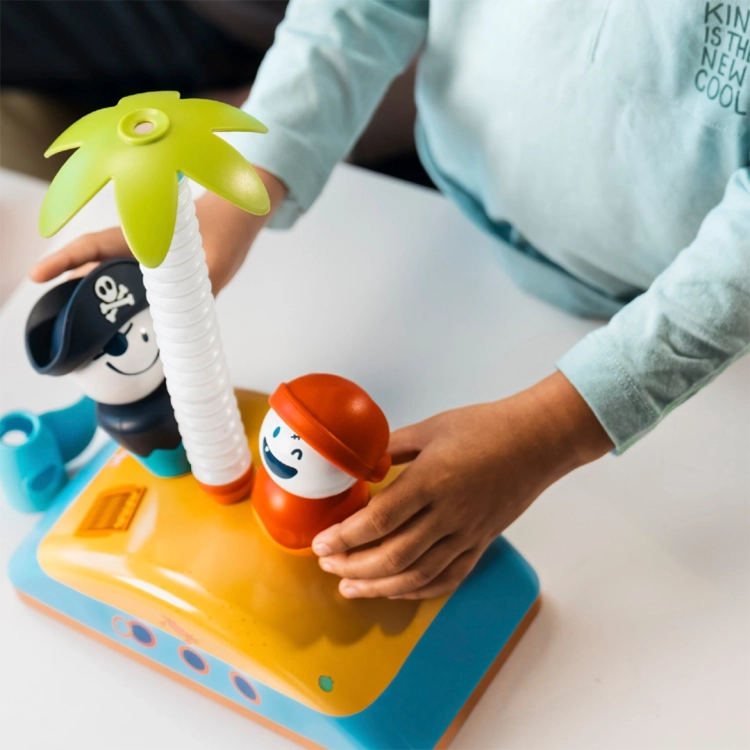 Dziecięce dłonie układające elementy magnetyczne na pokładzie statku, w tym maszt zakończony zieloną palmą.