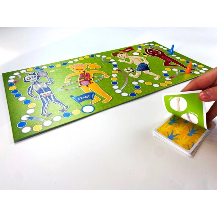 Rozłożona plansza gry Ciało człowieka z pionkami i talia kart. Widoczne ilustracje szkieletu, mięśni i organów oraz dłoń odkrywająca kartę.