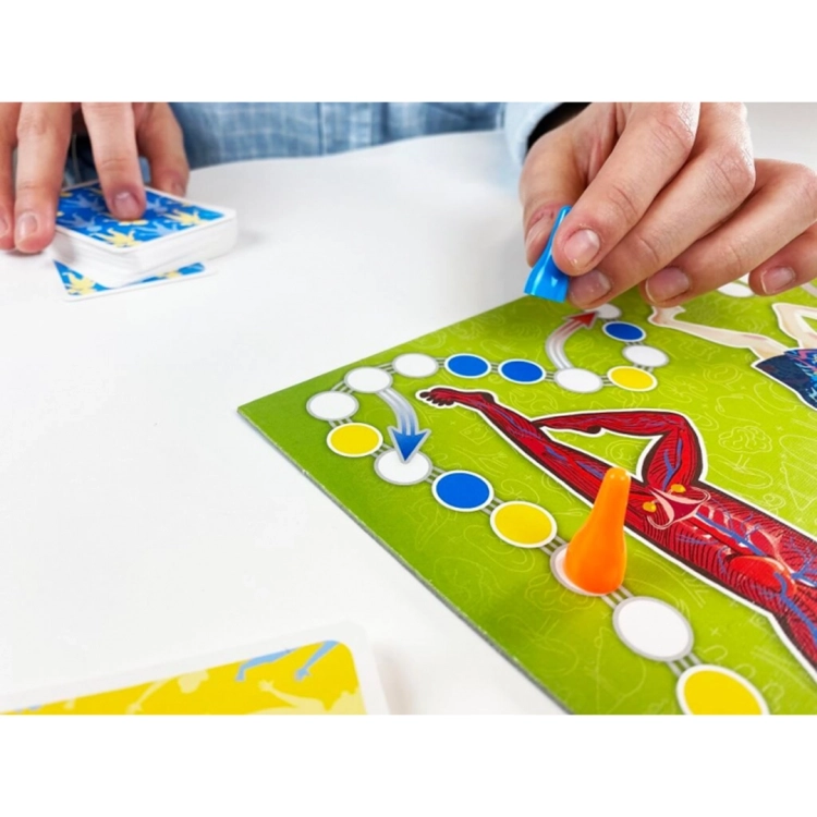 Zbliżenie na dłoń przesuwającą niebieski pionek po planszy gry. W tle talia kart, a na planszy grafika przedstawiająca ludzkie mięśnie.