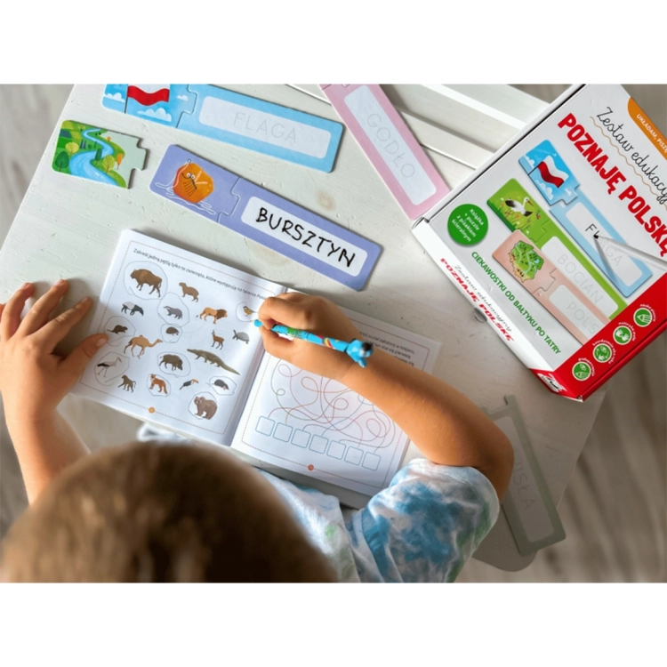 Dziecko wypełnia zadania w książeczce edukacyjnej. Obok leżą puzzle z obrazkami i polskimi słowami do odwzorowania: Flaga, Bursztyn.