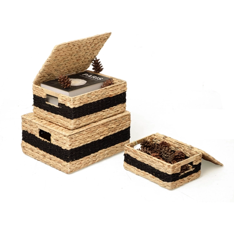 Trzy plecione kosze z hiacyntu wodnego z czarnym paskiem, ułożone w stos. W górnym znajduje się książka i szyszki, w najmniejszym – same szyszki.