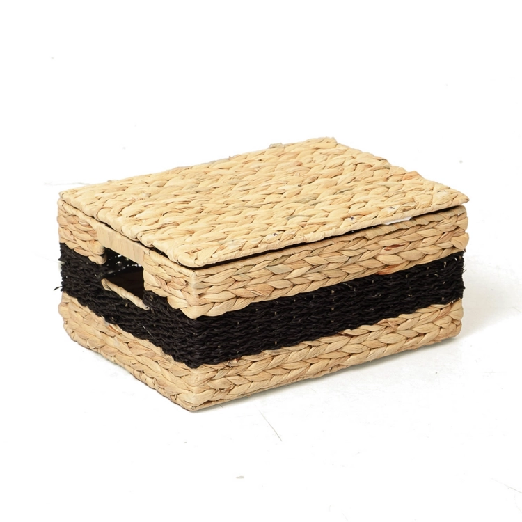 Prostokątny, pleciony kosz z hiacyntu wodnego z dopasowaną pokrywą, ustawiony pod kątem na białym tle. Organizer ma naturalny słomkowy kolor z kontrastującym czarnym paskiem pośrodku.