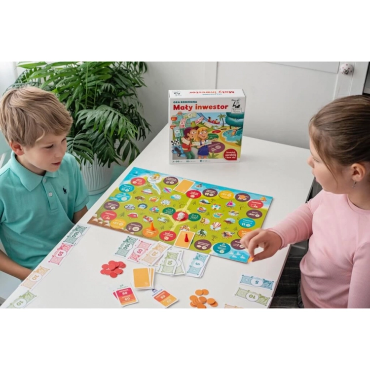 Chłopiec i dziewczynka grają przy stole w "Małego inwestora"; w tle widoczne pudełko gry oraz akcesoria do nauki przedsiębiorczości.