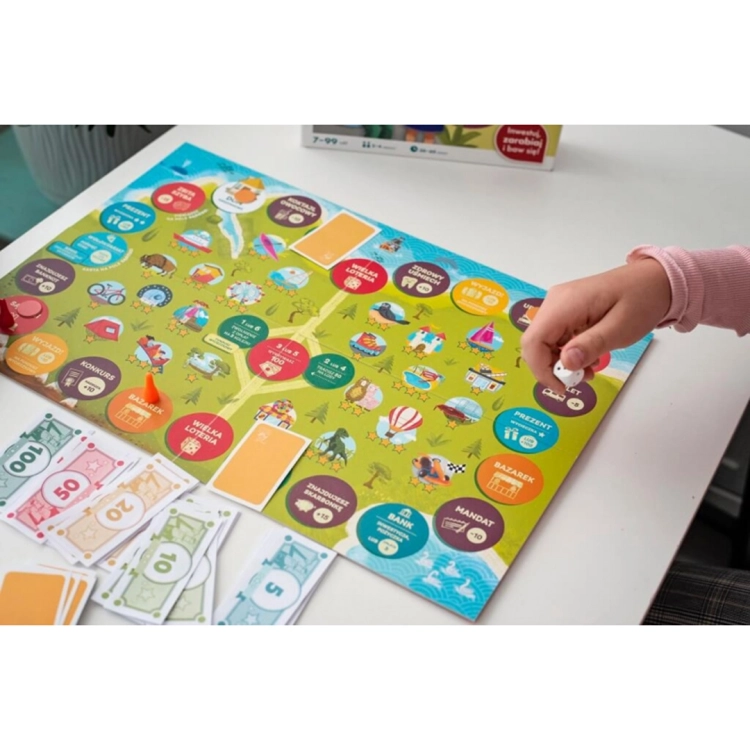 Detal dłoni rzucającej kostką na kolorową planszę gry; obok widoczne pionki w kształcie stożków oraz pliki zabawkowych pieniędzy.