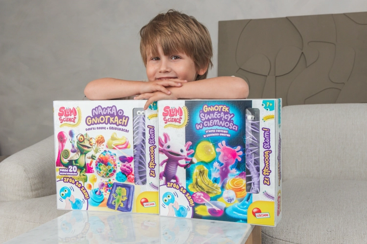 Chłopiec opierający się o dwa pudełka zestawów Slumi Science – Laboratorium gniotków oraz wersję świecącą w ciemności.