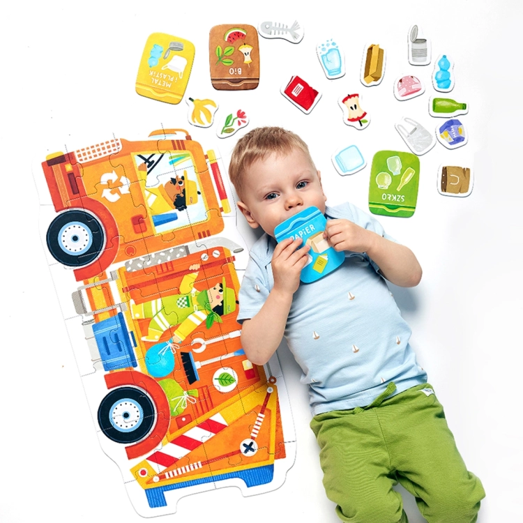 Chłopiec leży na białym tle obok ułożonych puzzli; trzyma w dłoniach element przedstawiający niebieski kontener na papier.