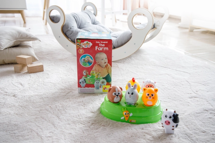 Widok na sorter z figurkami ustawiony na jasnym dywanie obok opakowania produktu i drewnianej bujawki w pokoju dziecięcym.