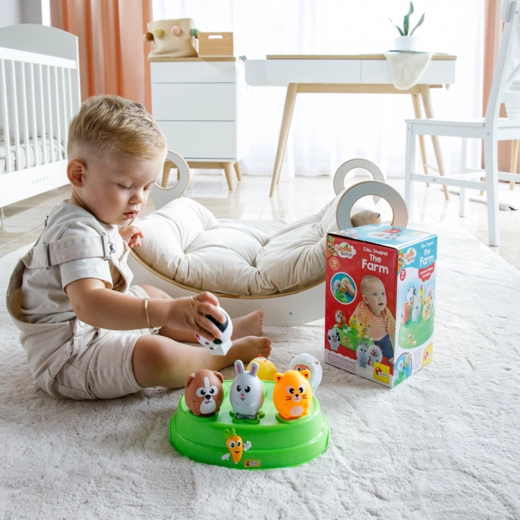 Dziecko siedzące na dywanie dopasowuje figurkę krowy do odpowiedniego otworu w zielonej podstawie sortera edukacyjnego.