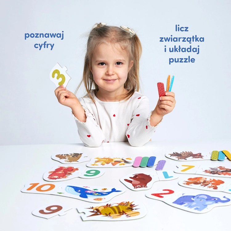 Uśmiechnięta dziewczynka prezentuje element puzzli z cyfrą 3 oraz kolorowe patyczki do nauki liczenia.