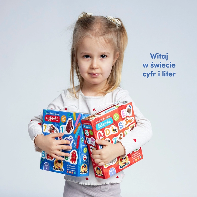 Dziewczynka trzyma w rękach dwa pudełka gier edukacyjnych CzuCzu: niebieskie „Cyferki” oraz czerwone „Literki”.