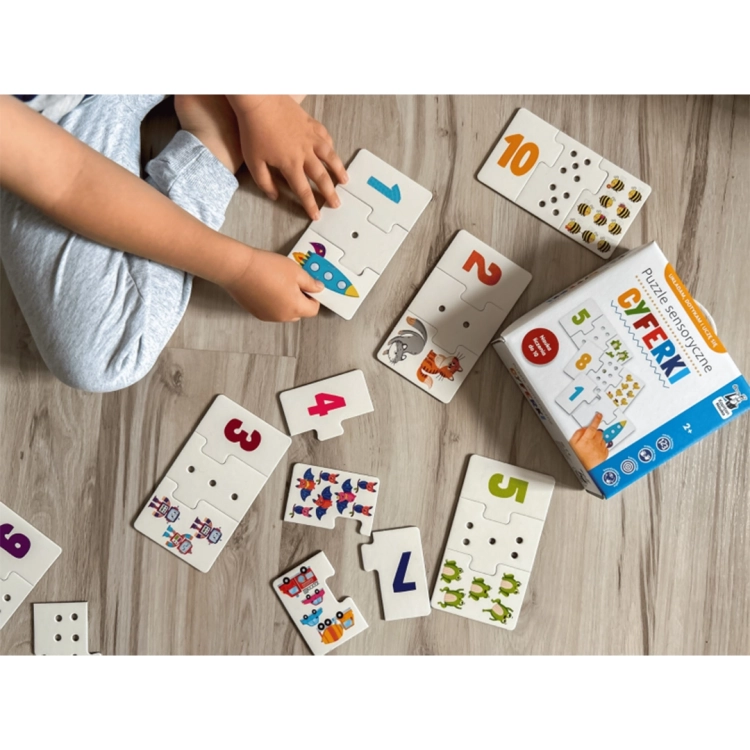Dziecko siedzące na podłodze układa puzzle sensoryczne z cyframi, obrazkami zwierząt i dziurkami do przeliczania.