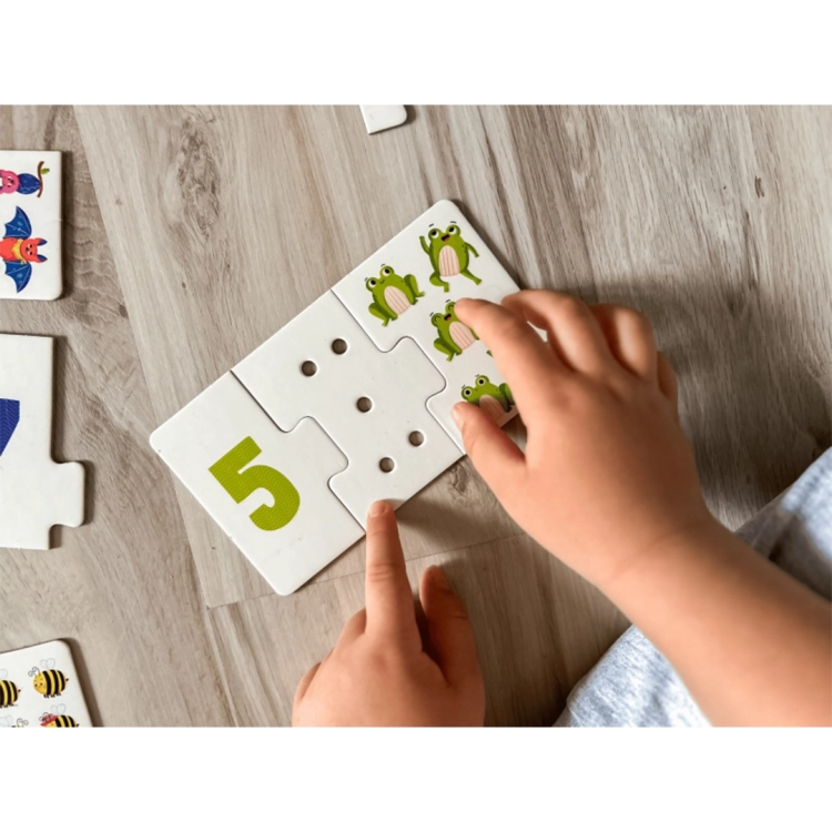 Dziecko siedzące na podłodze układa puzzle sensoryczne z cyframi, obrazkami zwierząt i dziurkami do przeliczania.