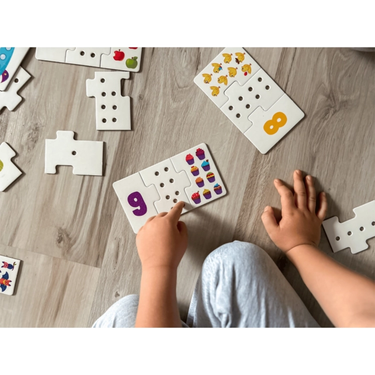 Dziecko przelicza dziurki na środkowym elemencie puzzli obok cyfry 9 i obrazka z kolorowymi babeczkami.