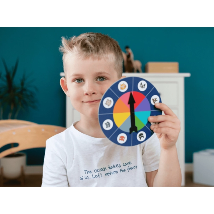 Uśmiechnięty chłopiec trzyma przed sobą okrągłą tarczę losującą z kolorowymi polami i wizerunkami kotów.